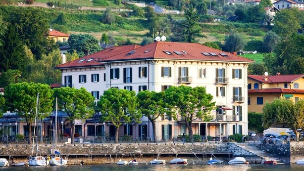 A waterfront building with multiple balconies, a stone staircase leading to the entrance, and several boats docked in the water. - Albergo Lenno (Tremezzina)