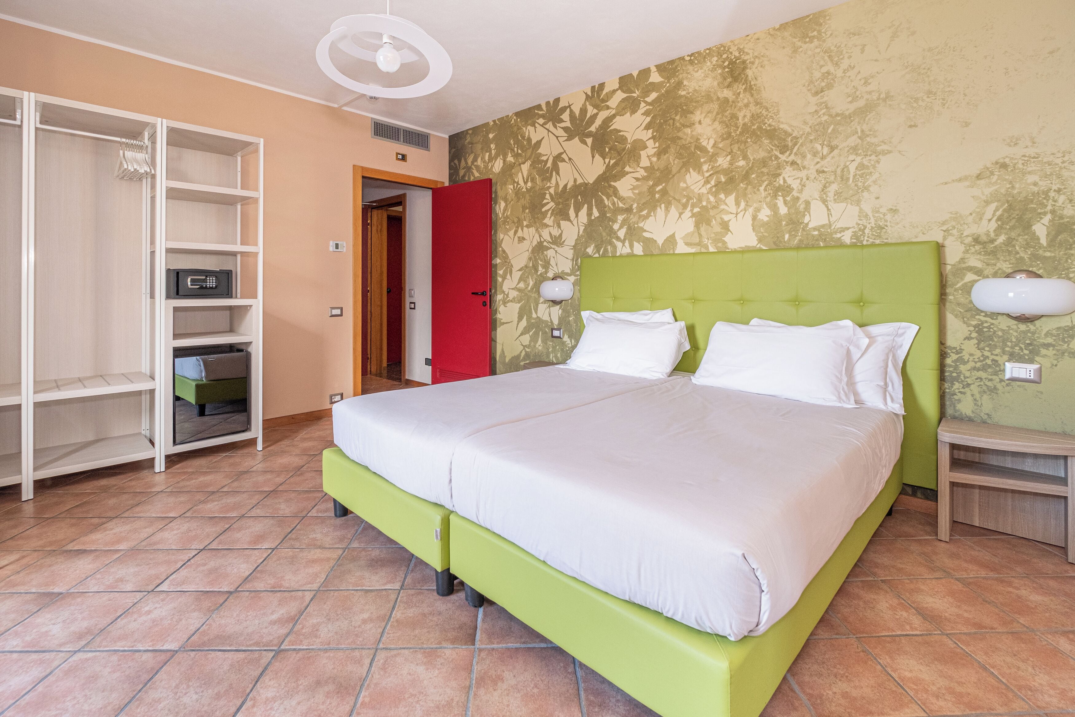 A bedroom with a green bed, white bedding, a wardrobe, and a red door.