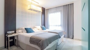 Una habitación de hotel moderna con dos camas, una mesita de noche con teléfono y un gran ventanal con cortinas.