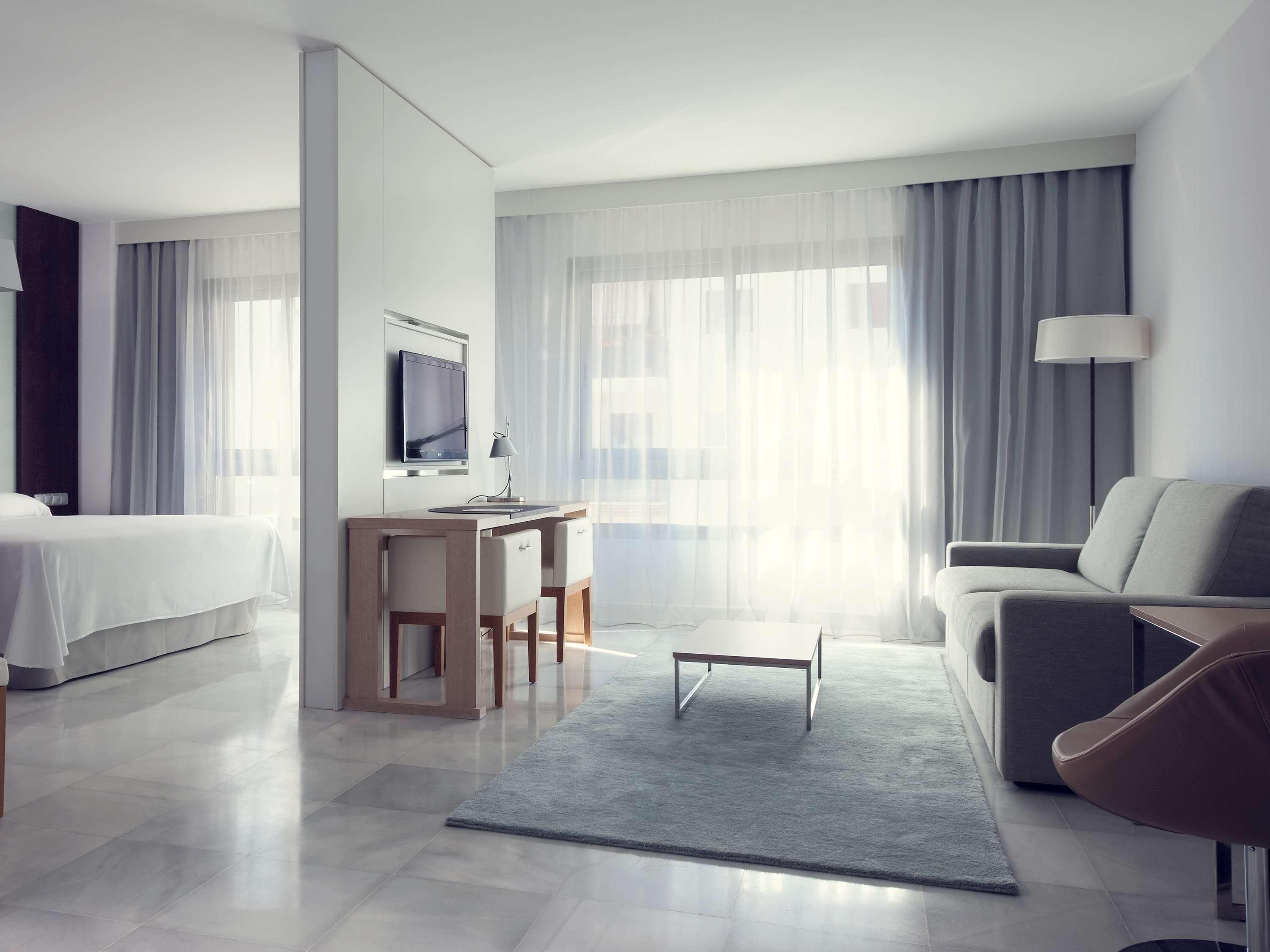 A modern hotel room with a bed, a desk, a sofa, and a TV.