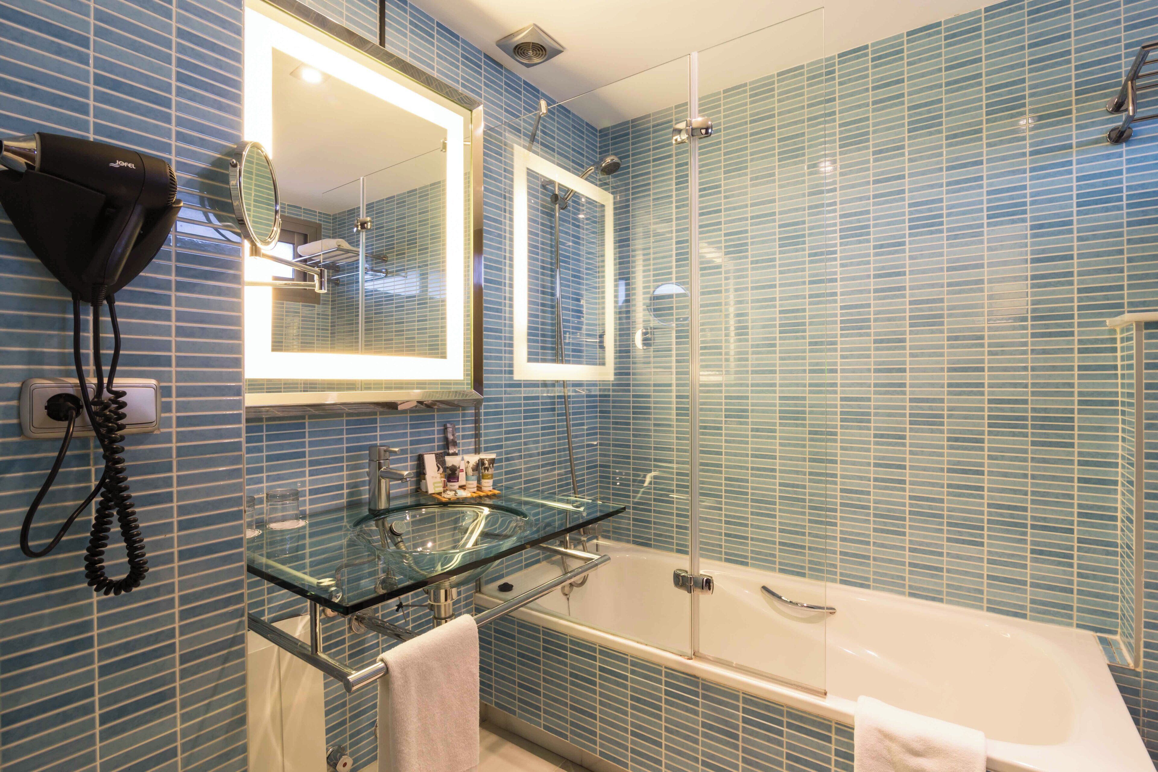 A bathroom with a glass vanity, a large mirror, a shower enclosure, and a bathtub.