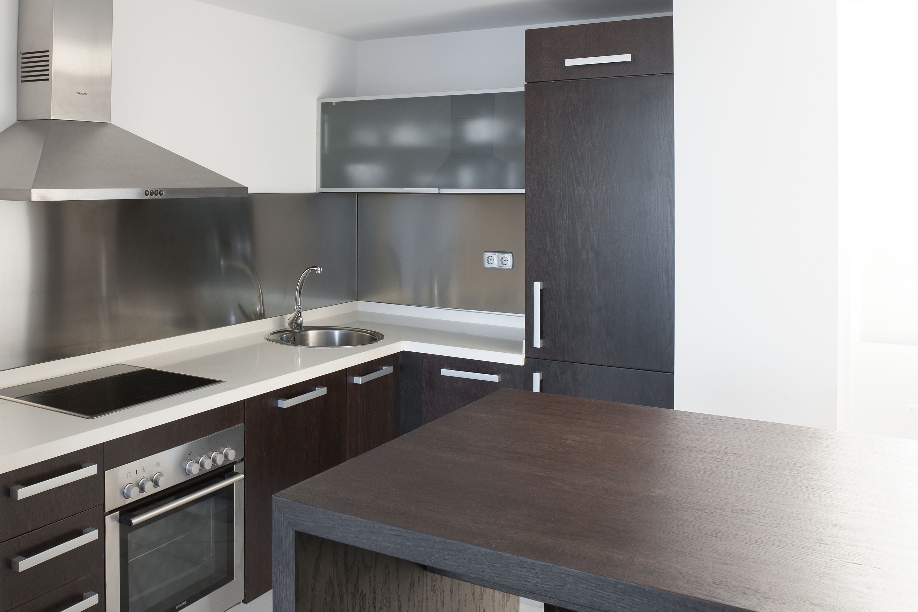 A modern kitchen with stainless steel appliances, a built-in oven, and a dark wooden countertop.