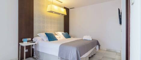 Habitación de hotel moderna con una cama grande, una mesita de noche, una lámpara de pared y un enchufe visible.