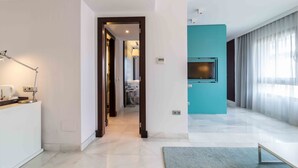 Habitación de hotel moderna con un ventanal grande, un televisor de pantalla plana montado en la pared, un escritorio con lámpara y un baño visible a través de una puerta abierta.