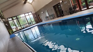 Una piscina interior con agua cristalina, suelo de baldosas y vistas al exterior a través de amplios ventanales.
