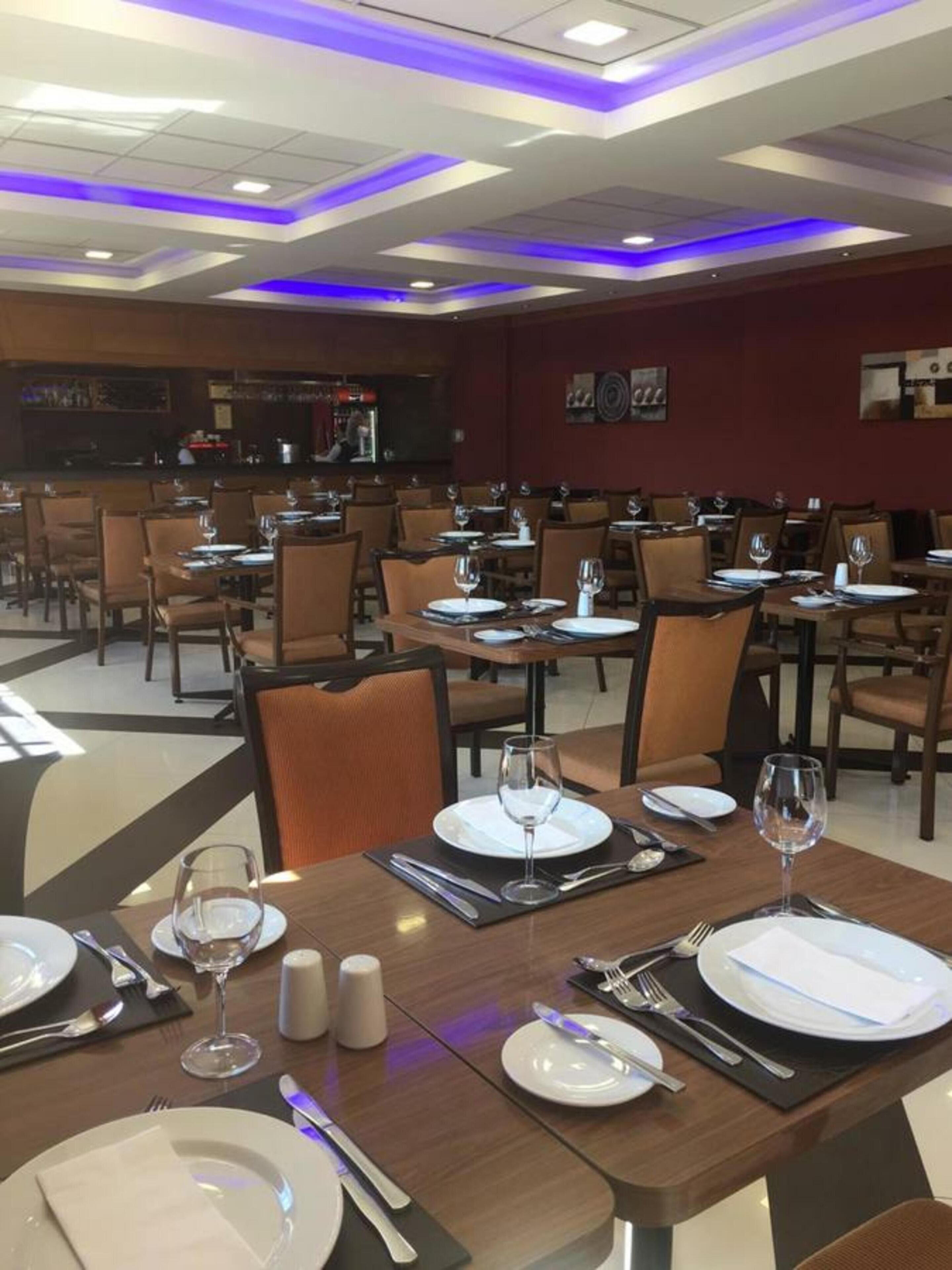 A restaurant with multiple tables set for dining, featuring a modern ceiling design with blue lighting.