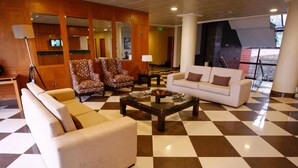 Un hall con suelo a cuadros, un sofá, sillones, una mesa de centro y una lámpara.