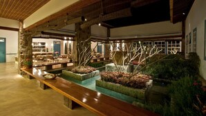 A spacious lobby with a long wooden bench, a small water feature, and potted plants.