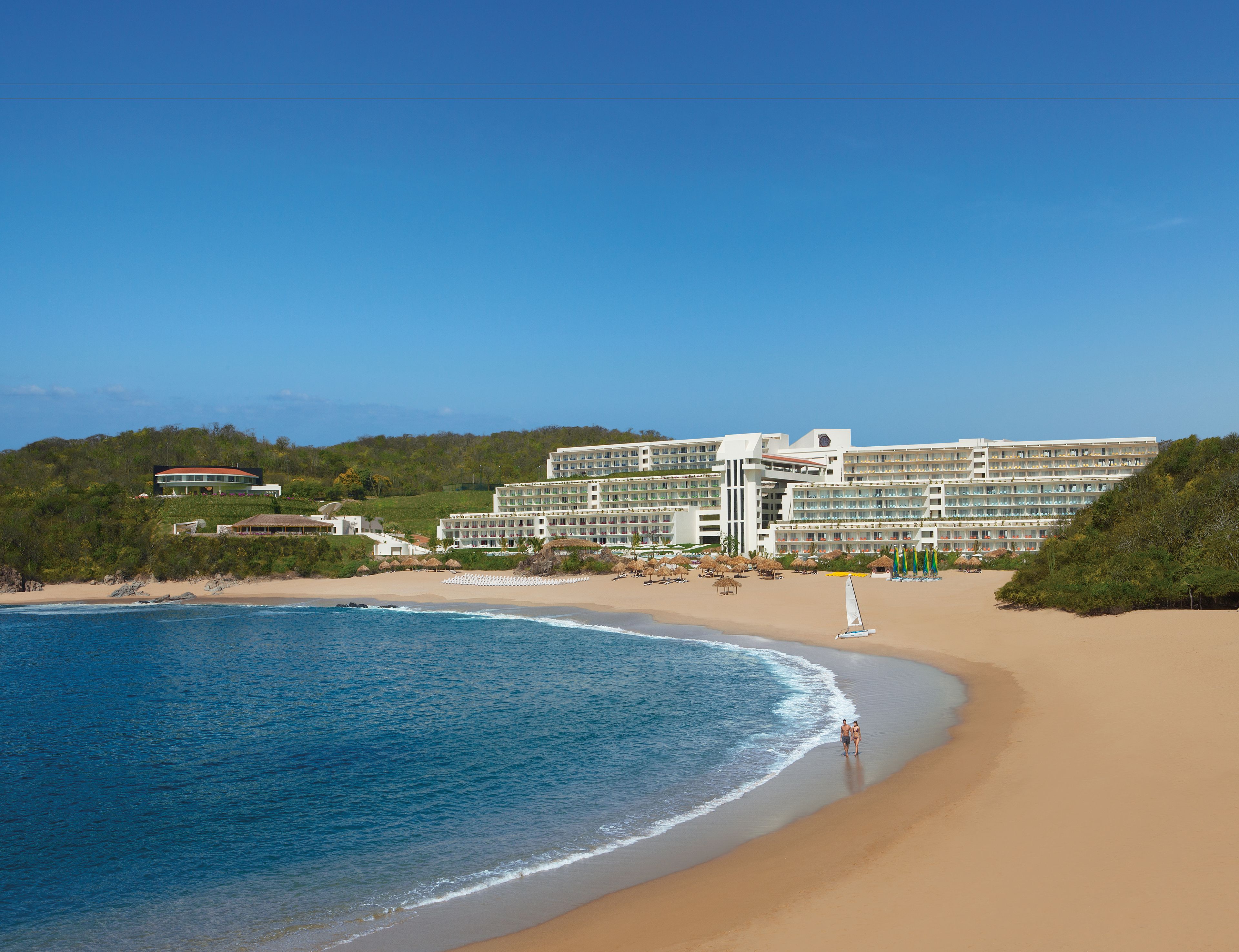 Ein Hotel direkt am Strand mit mehreren Etagen, ein Strand mit Sonnenschirmen und freiem Blick auf den Ozean.