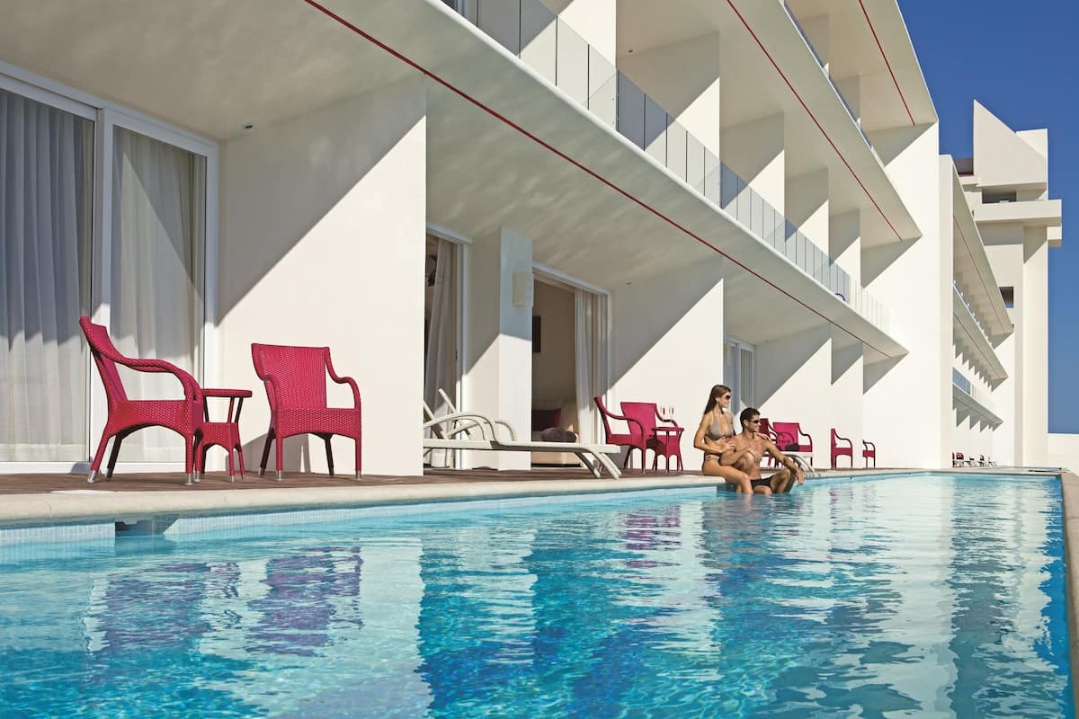Ein Swimmingpool mit roten Liegestühlen und ein weißes Gebäude mit Balkonen.