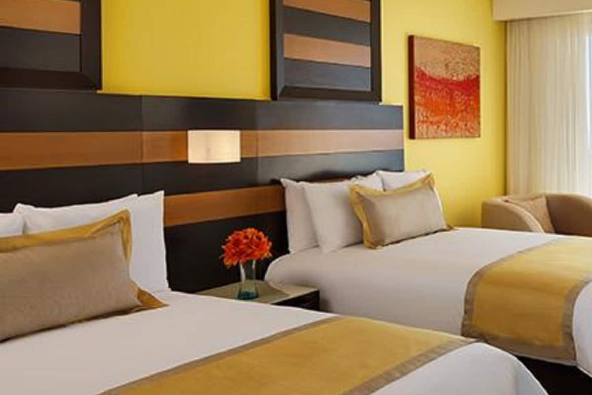 Ein Hotelzimmer mit zwei Betten, einem Holzkopfteil, einer gelben Akzentwand und einem Gemälde.