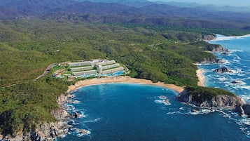 Vue aérienne d’un complexe hôtelier comprenant plusieurs bâtiments, une plage et une côte.