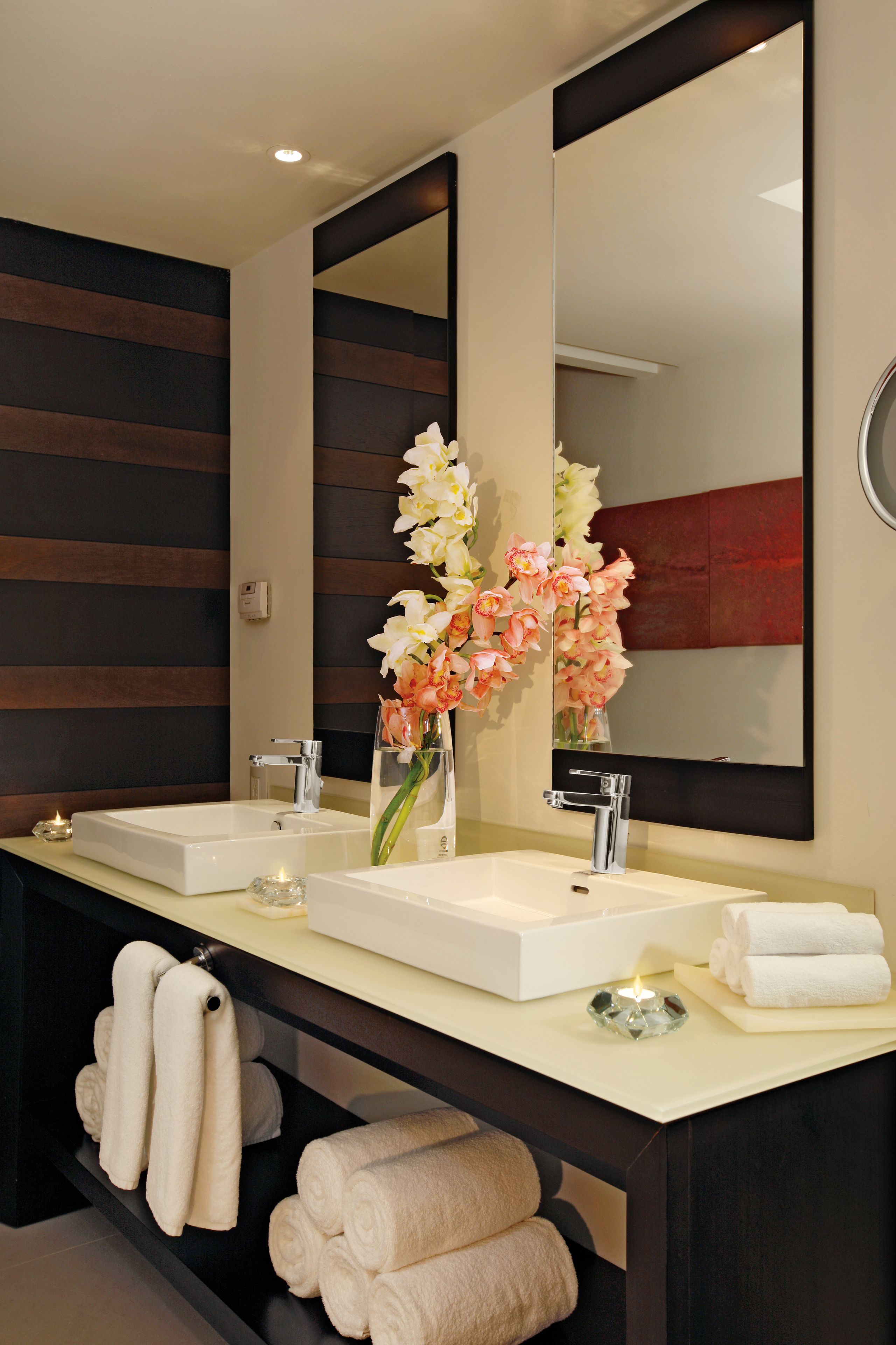 A modern bathroom with two sinks, a large mirror, and a vase of flowers.