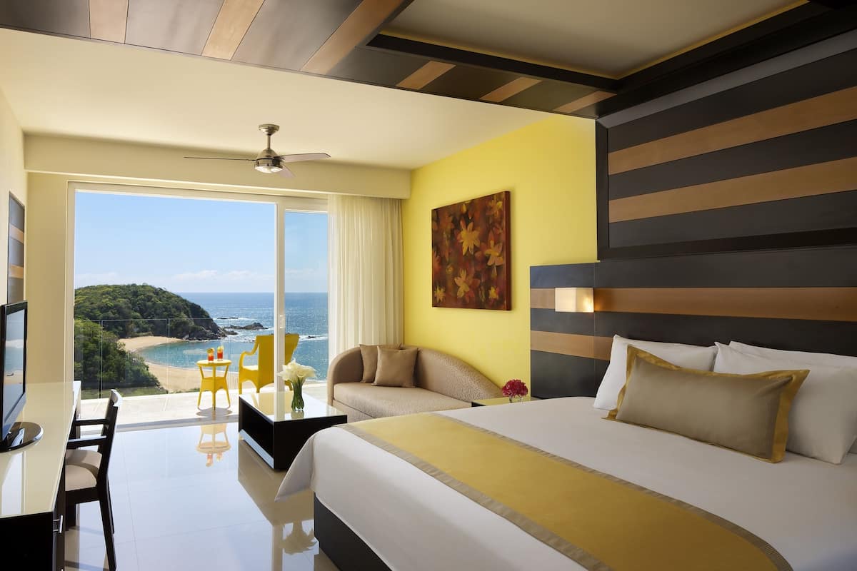 Ein Hotelzimmer mit einem großen Bett, einem Schreibtisch, einem Stuhl und Blick auf das Meer.