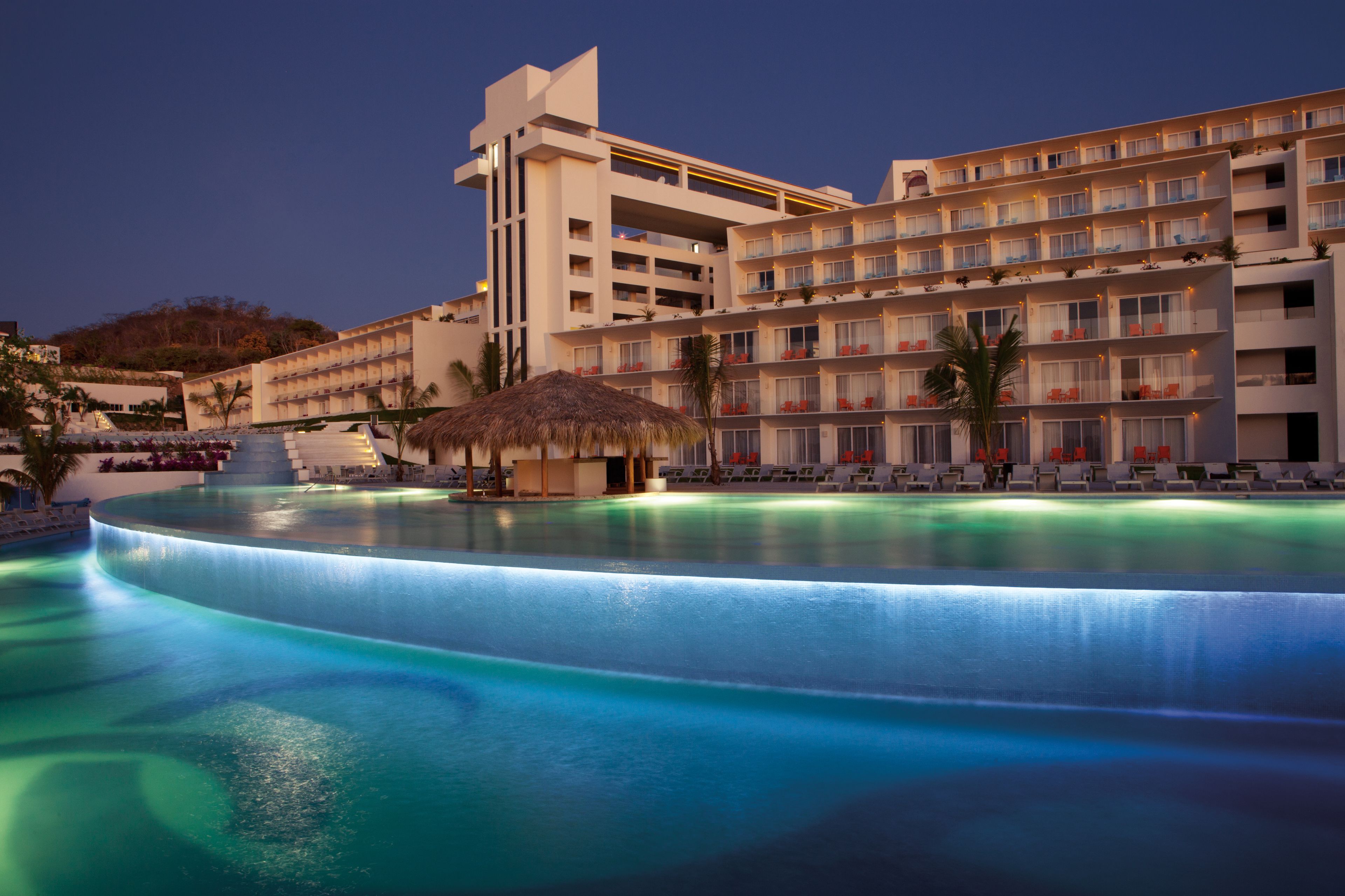 Ein Hotel mit großzügigem Infinity-Pool, mehreren Balkonen und einem Gebäude mit Strohdach.