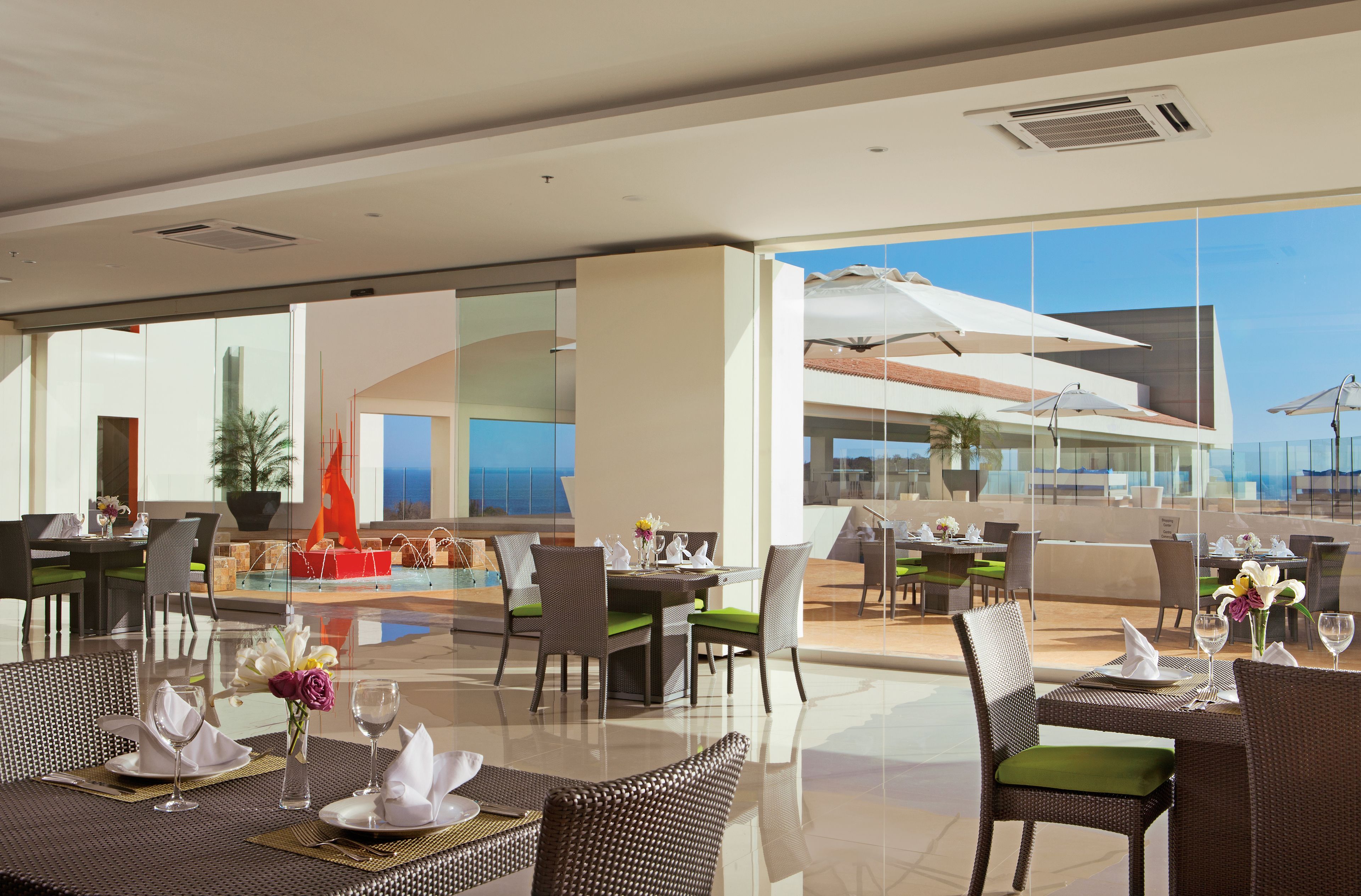 A modern outdoor dining area with tables and chairs, a pool, and a view of the ocean.