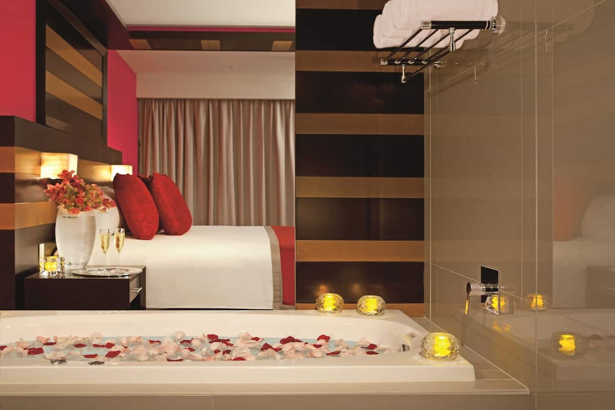 Ein modernes Hotelzimmer mit einem großen Bett, einer Badewanne mit Rosenblättern und Kerzen auf dem Nachttisch.