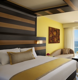 Une chambre d’hôtel avec un grand lit, un canapé, un tableau et une vue sur l’océan.