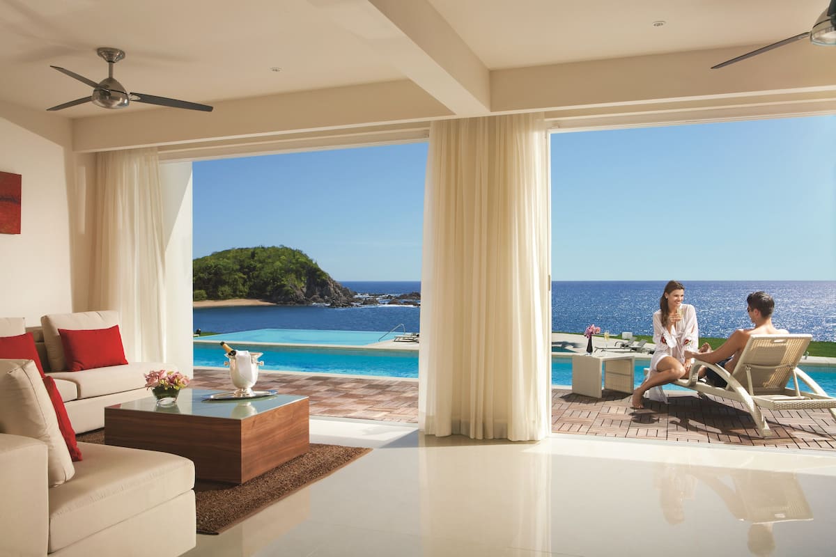 Ein modernes Wohnzimmer mit großem Fenster mit Blick auf Pool und Meer.