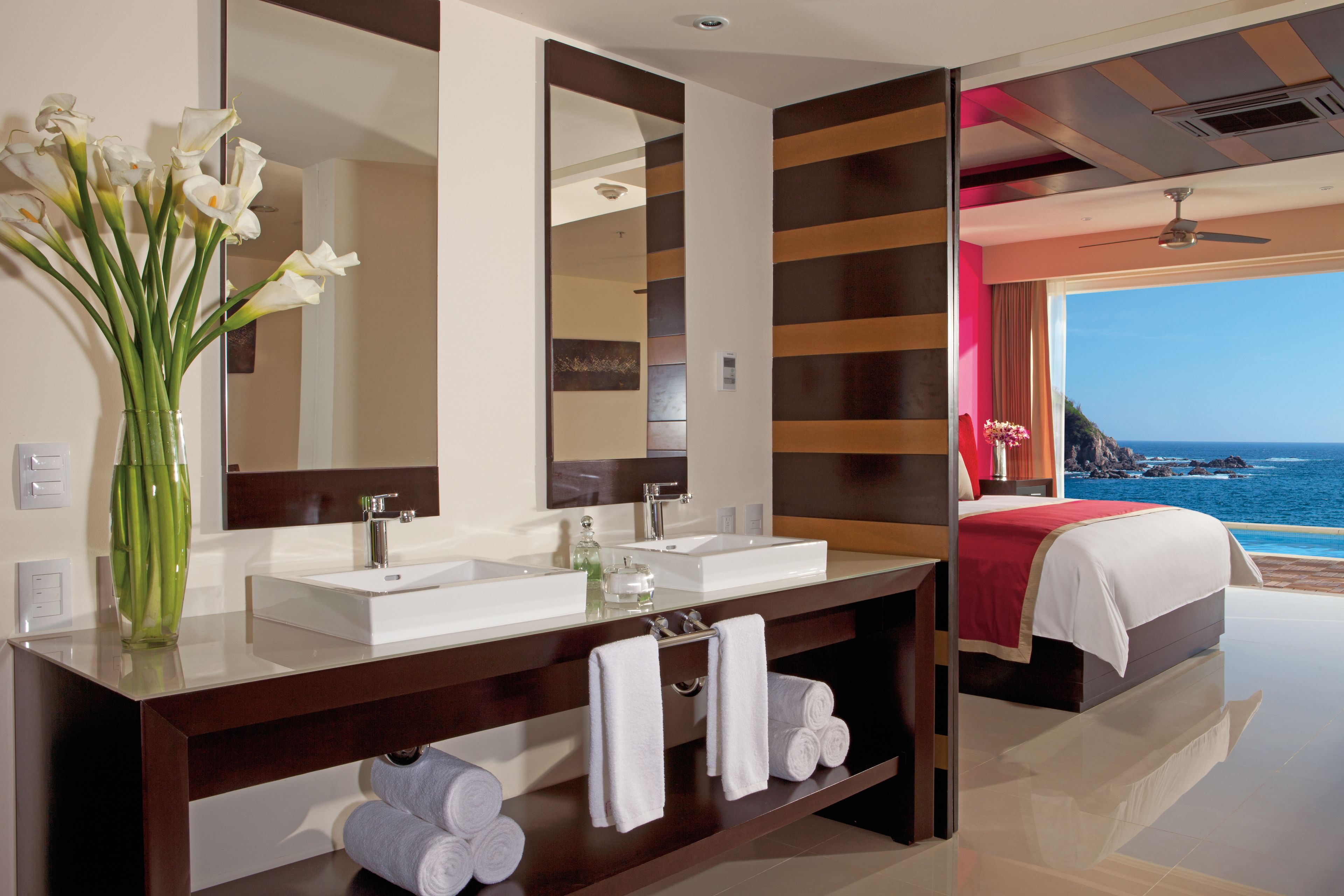 A modern bathroom with dual sinks, a large mirror, and a view of the ocean.