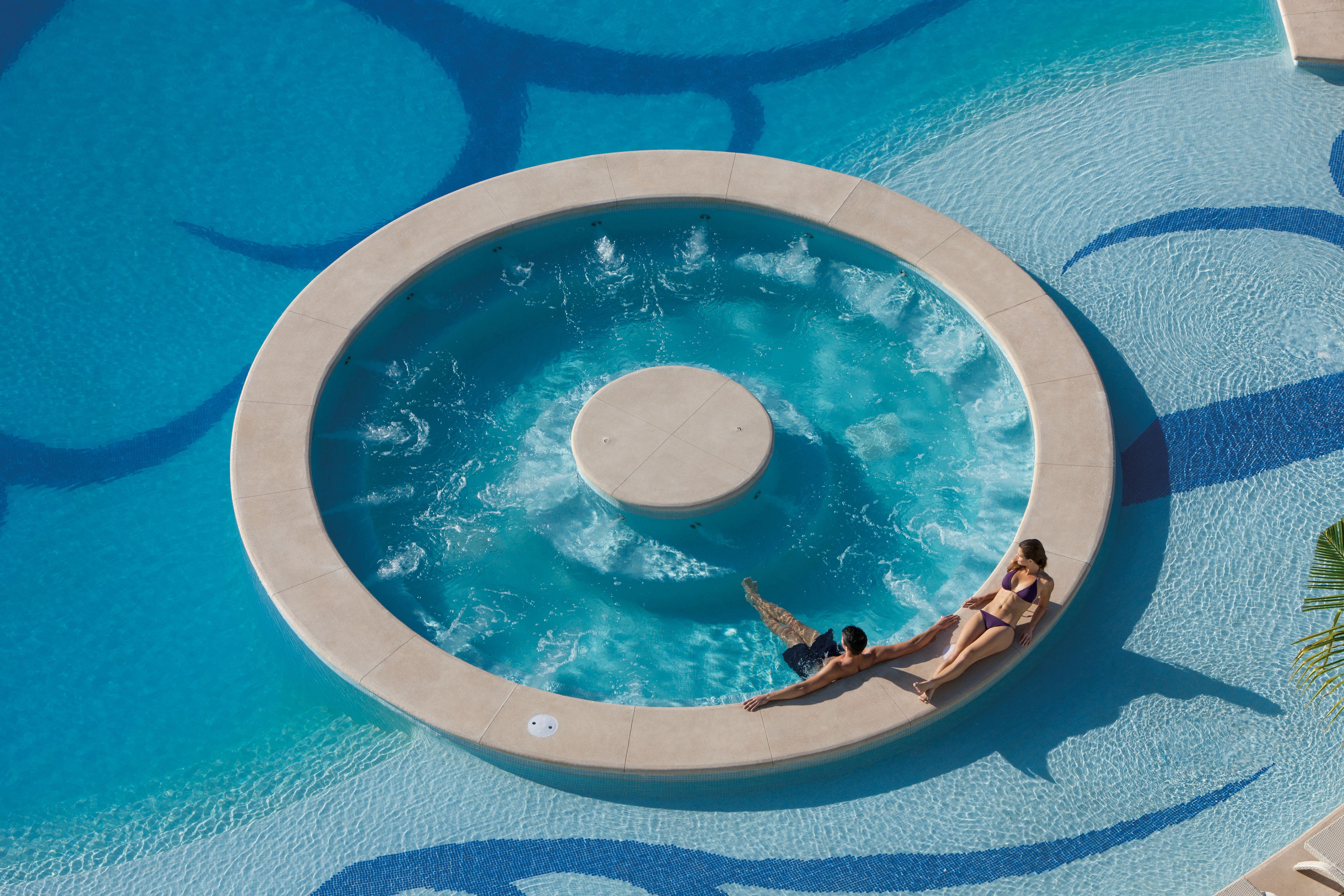 A circular infinity pool with a central water feature, surrounded by a tiled deck.