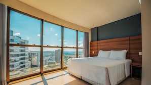 A modern hotel room with a large bed, wooden headboard, and a city view through floor-to-ceiling windows. - Laghetto Bento (Bento Gonçalves)