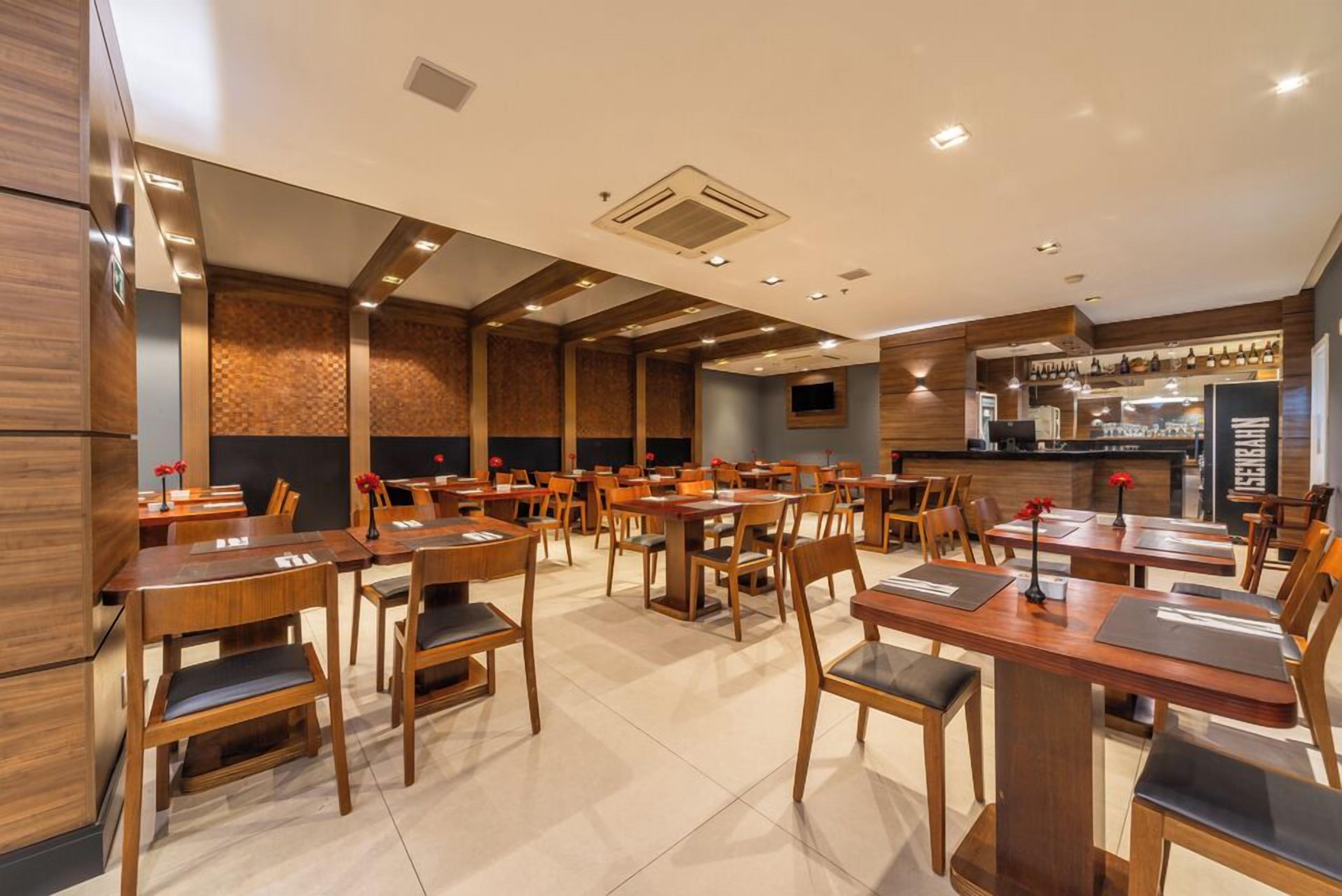 Un restaurante con mesas y sillas de madera, una zona de bar y una barra con un menú.