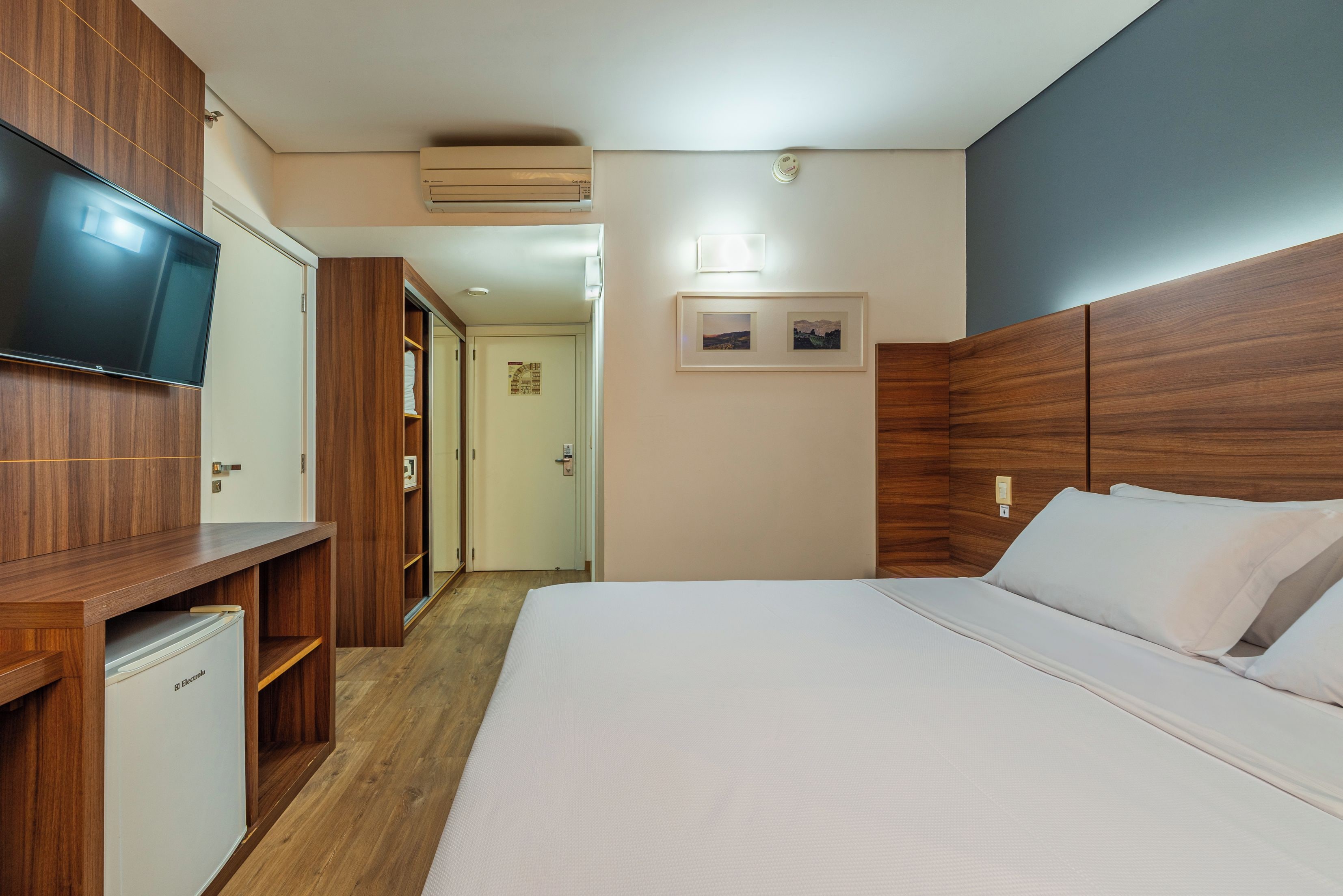 Ein Hotelzimmer mit Bett, Fernseher, Kleiderschrank und kleinem Kühlschrank.