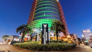 A tall hotel with a curved facade, a prominent sign, and palm trees in the foreground. - Laghetto Bento (Bento Gonçalves)