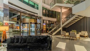 A modern lobby with a black sofa, a staircase, and a glass elevator. - Laghetto Bento (Bento Gonçalves)
