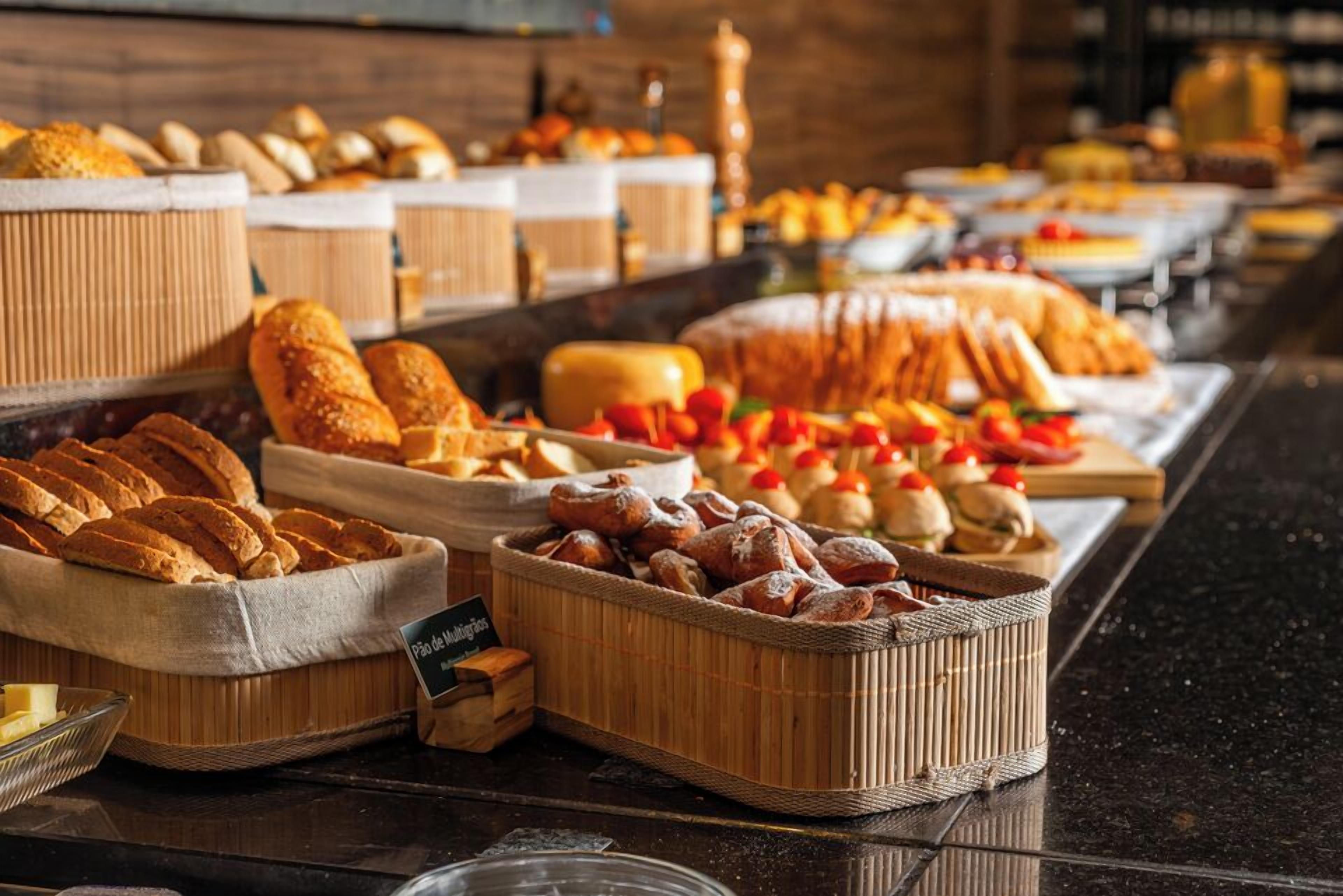 Um buffet com diversos pães, pastelaria e frutas.