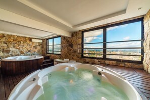 Zona de spa con dos jacuzzis, paredes de piedra y ventanas amplias con vistas a la ciudad.