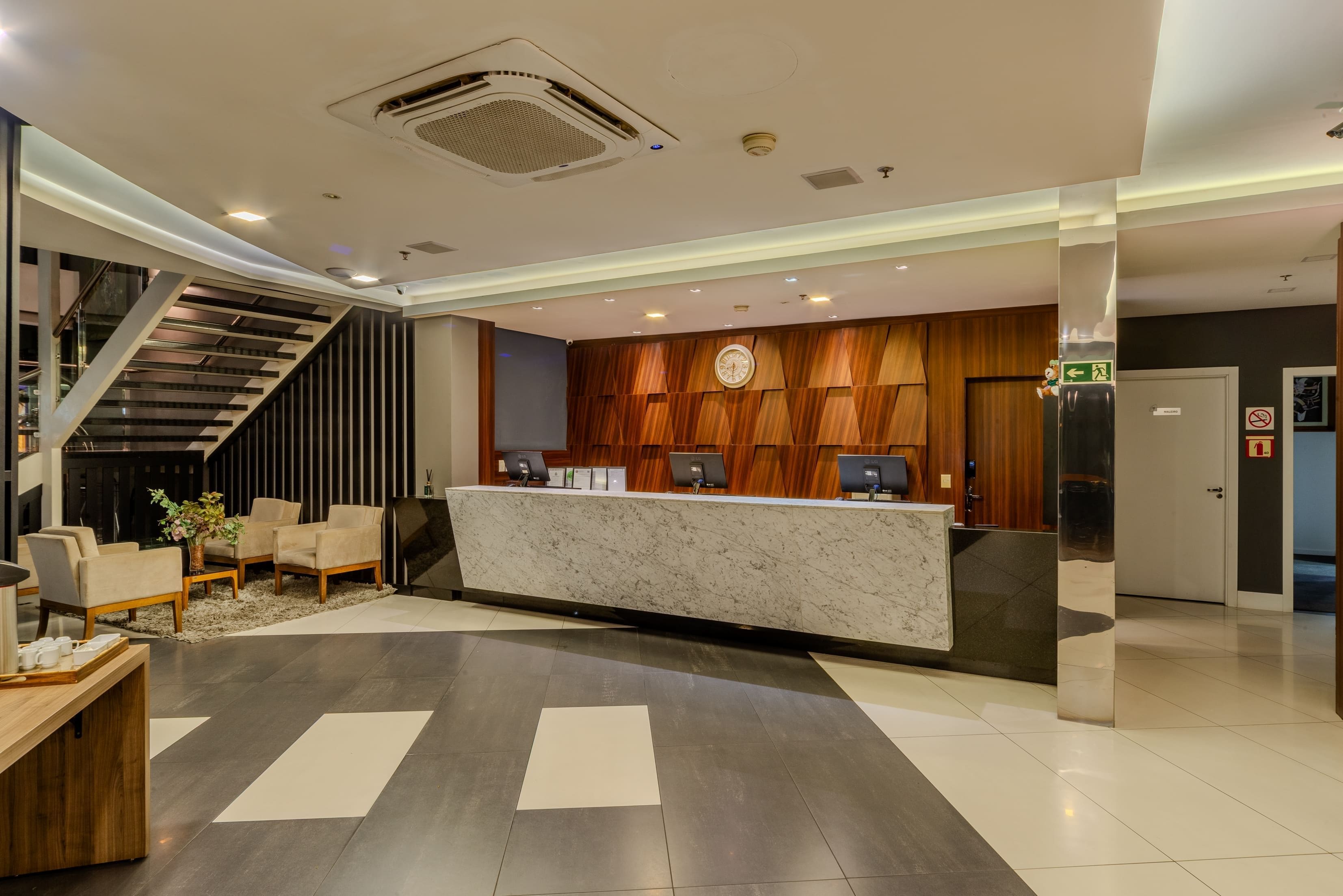 A modern reception area with a marble counter, a wooden panel wall, and a staircase.