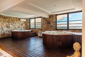 Une salle de spa avec des murs en pierre, un plancher en bois et deux bains à remous.