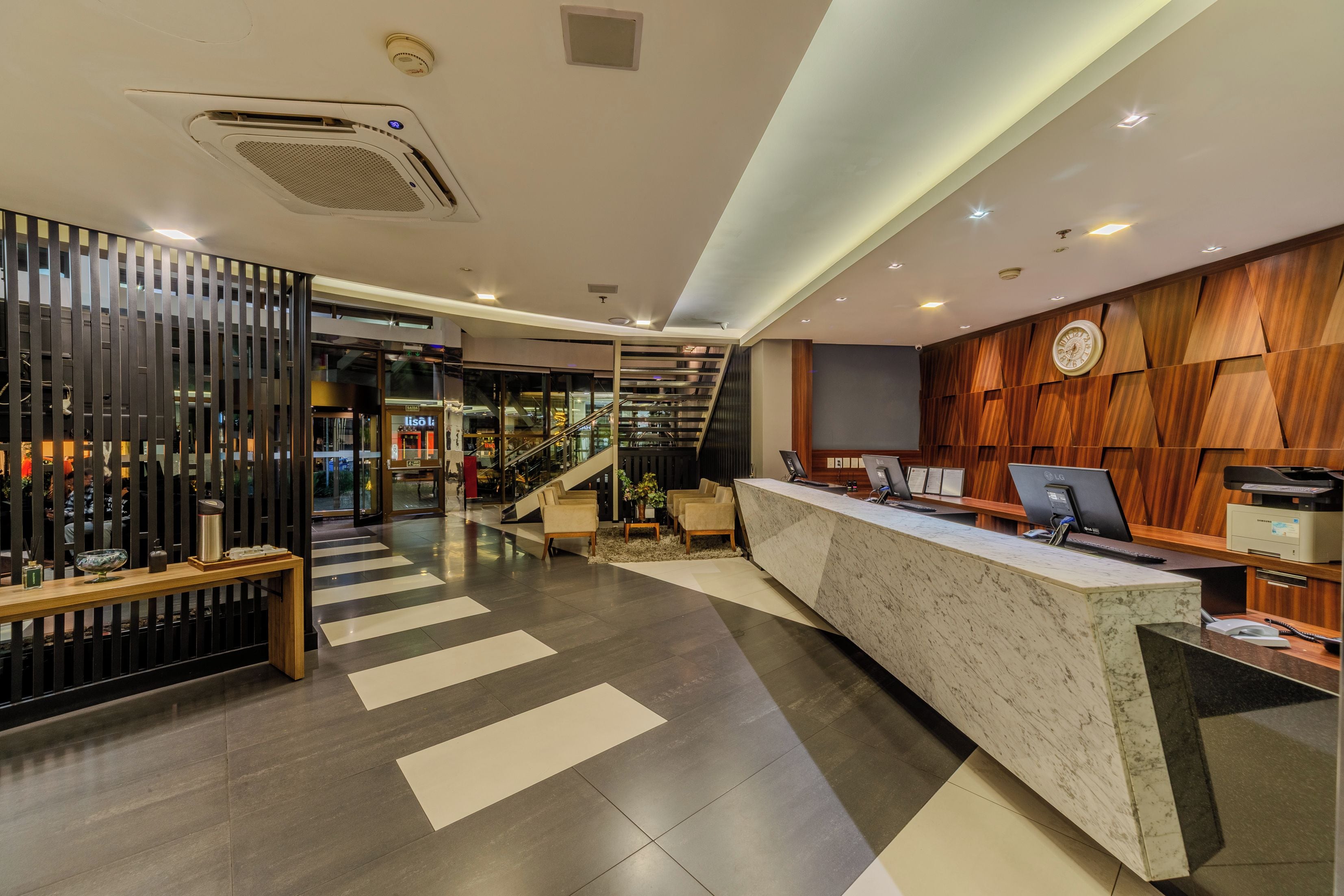 A hotel reception area with a modern design, including a reception desk, seating area, and a staircase leading to upper floors.