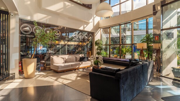 A spacious lobby with a modern design, featuring a large seating area, a coffee shop, and large windows allowing natural light. - Laghetto Bento (Bento Gonçalves)