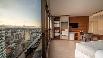 Quarto de hotel moderno com uma grande janela, uma cama, uma escrivaninha e um guarda-roupa.
