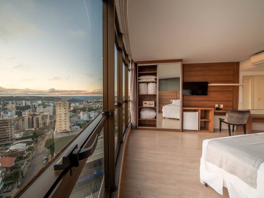 Una habitación de hotel moderna con un ventanal grande, una cama, un escritorio y un armario.