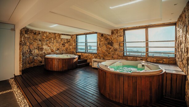 A spa area with two wooden hot tubs, stone walls, and large windows offering a view. - Laghetto Bento (Bento Gonçalves)