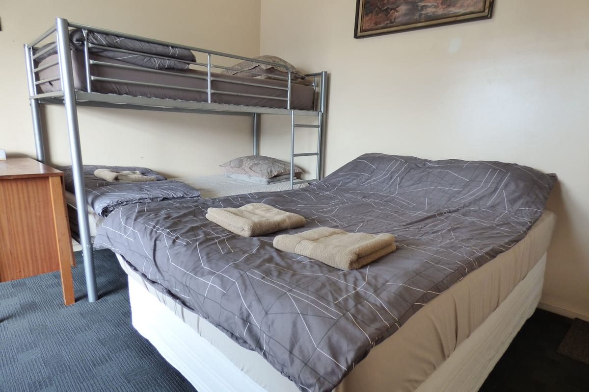 A bunk bed with a grey and white quilt, a wooden desk, and a framed picture on the wall.