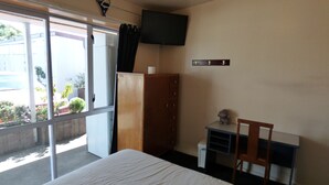 A hotel room with a bed, a desk, a chair, a television, and a wardrobe. - Racecourse Backpackers Hostel (Christchurch)