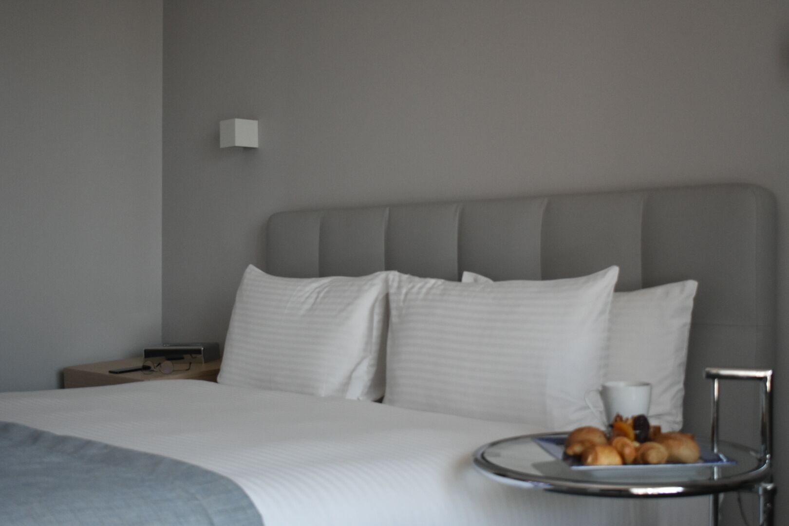 A hotel room with a large bed, a bedside table, a lamp, and a tray with pastries.