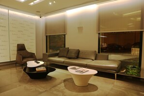 Relax in style with a comfortable armchair and sofa, surrounded by a sleek coffee table and floor-to-ceiling windows offering a view of the parking area.