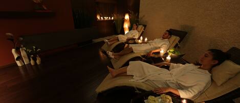 A spa room with two reclining chairs, candles, and a tray with fruits and a bowl of soup.