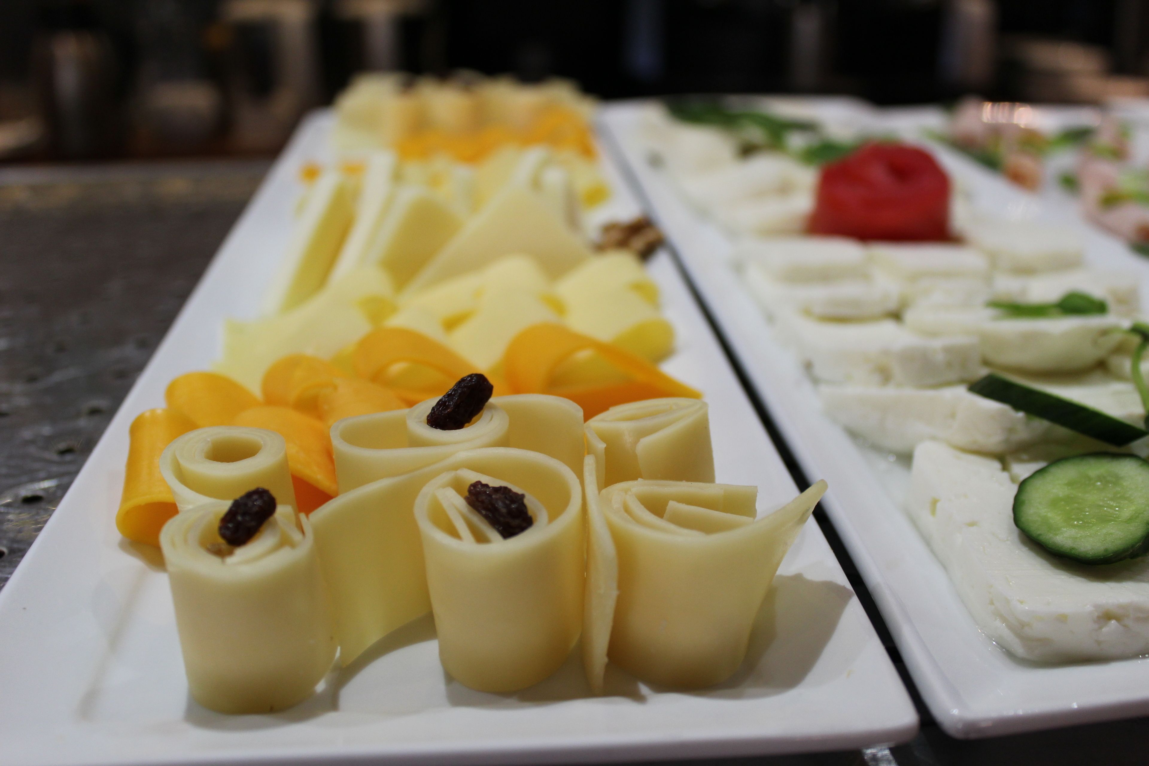 Un plat rectangular blanc amb diferents aliments, com formatge en rotlles, fruita tallada i un objecte vermell.