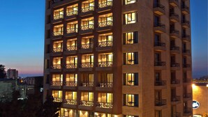 A multi-story hotel with illuminated windows and balconies, a parking area with several cars, and a view of the surrounding area. - ParkTower Suites (Beirut)