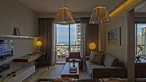 A modern living room with a sofa, coffee table, and TV. There is a balcony with a view of the city. - ParkTower Suites (Beirut)