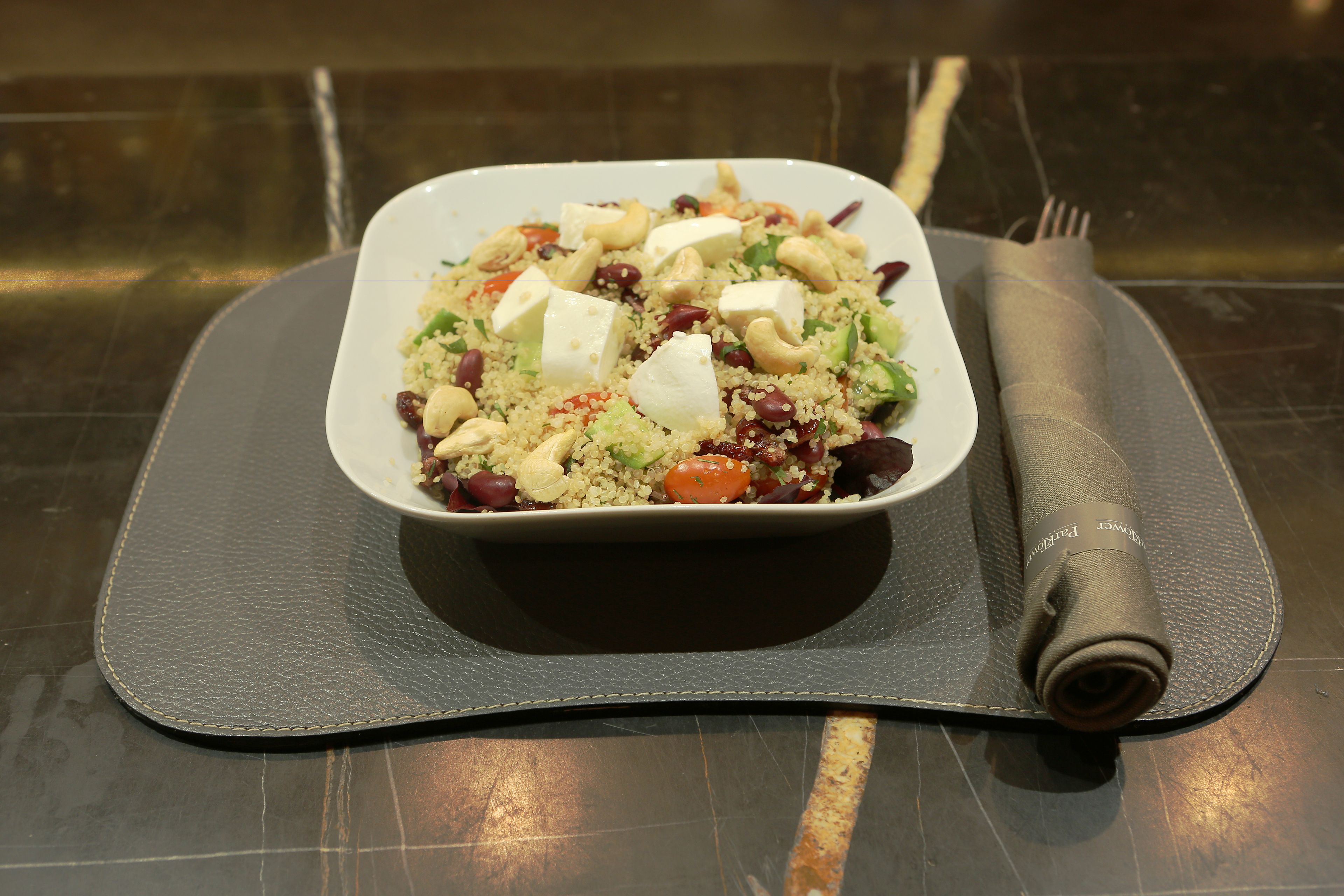 A square white plate with a salad on a dark textured mat.