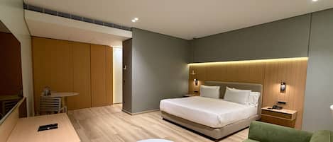 A modern hotel room with a bed, a green sofa, a round table, and a desk with a phone.