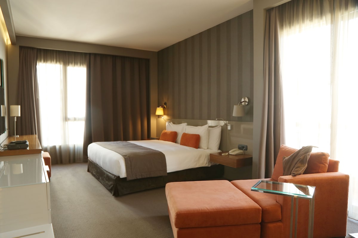 A hotel room with a bed, a desk, a chair, and a nightstand.